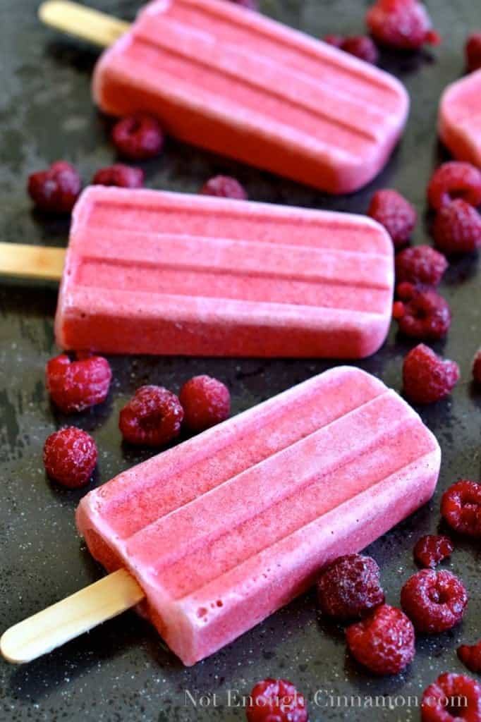 Coconut Berry Popsicles on a black tabletop surrounded by fresh raspberries - popsicles recipe 