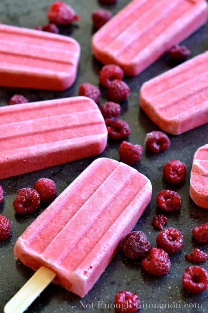 Coconut Berry Popsicles on a black tabletop surrounded by fresh raspberries