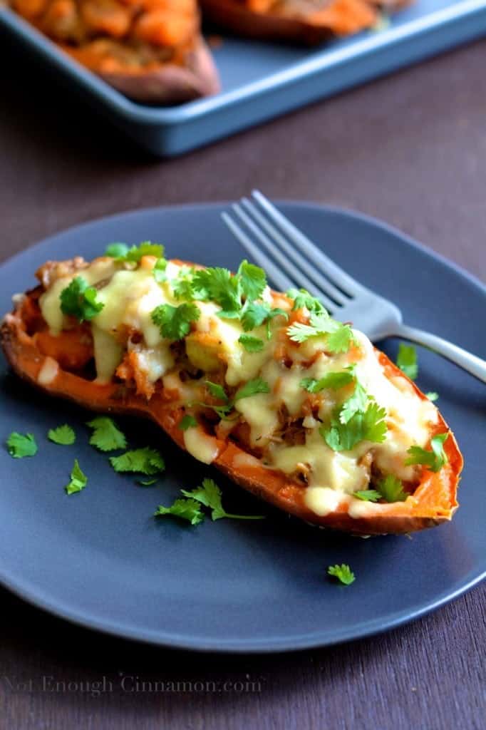 Pulled Pork Stuffed Sweet Potatoes with melted cheese and cilantro served on a blue plate with more sweet potato boats in the background