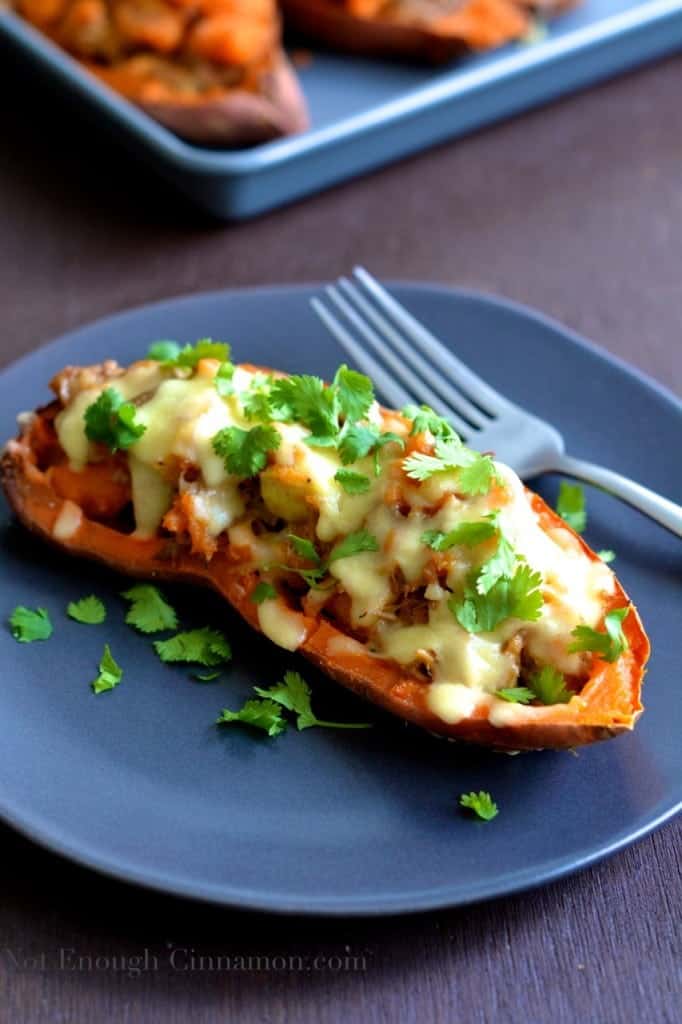 Pulled Pork Stuffed Sweet Potatoes with melted cheese and cilantro served on a blue plate with more sweet potato boats in the background