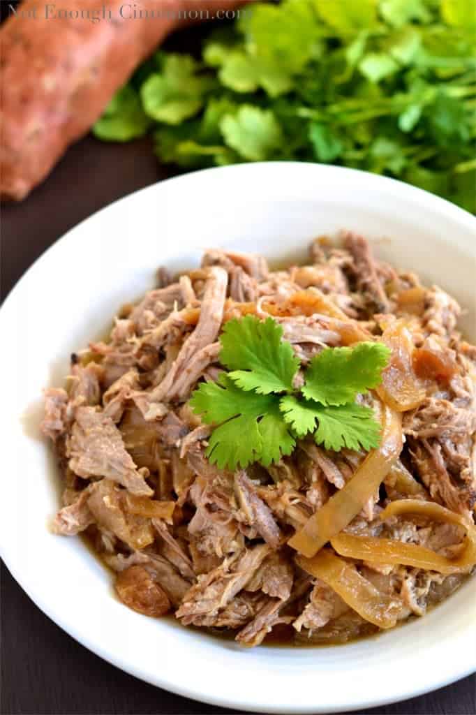 Slow Cooker Pulled Pork with Apples and Onions served in a white bowl with a fresh cilantro leave on top