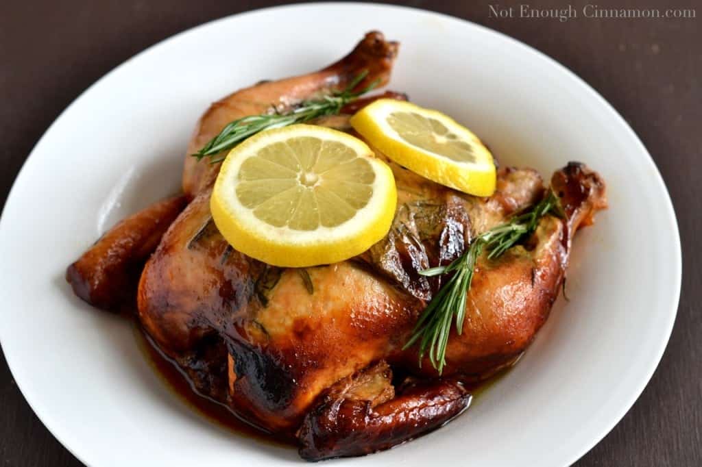 a big white bowl with a nicely browned Slow Cooker Whole Chicken with lemon slices and rosemary srpigs