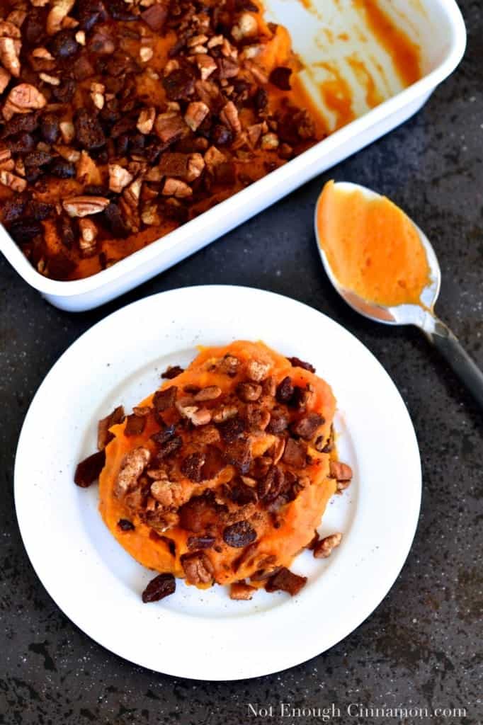  a small white plate of Sweet Potato Casserole with Pecans, Cranberries and Bacon on top in front of a half empty casserole dish