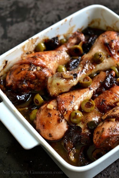Chicken Marbella made with chicken drumsticks served in a casserole dish with olives, prunes and capers nestled in between the chicken pieces