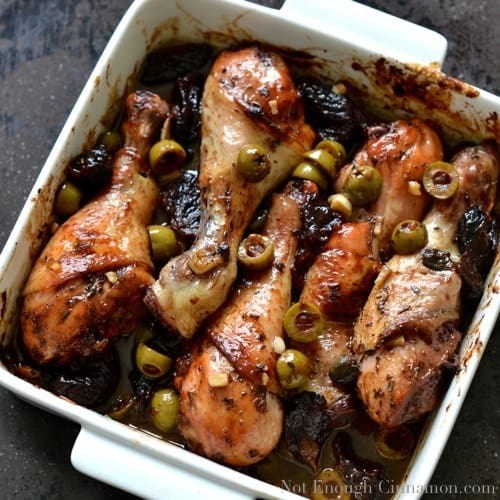 Chicken Marbella served in a white casserole olives and prunes nestled in between the chicken drumsticks