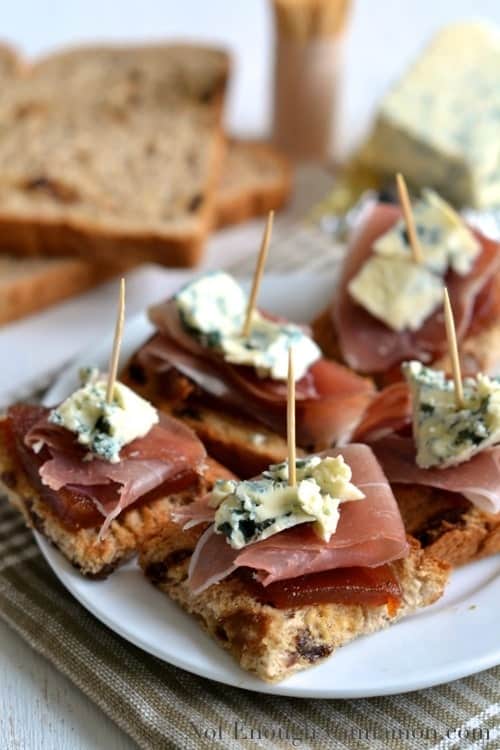 Quince, Prosciutto and Blue Cheese Toast bites arranged on a white plate and held together with toothpicks