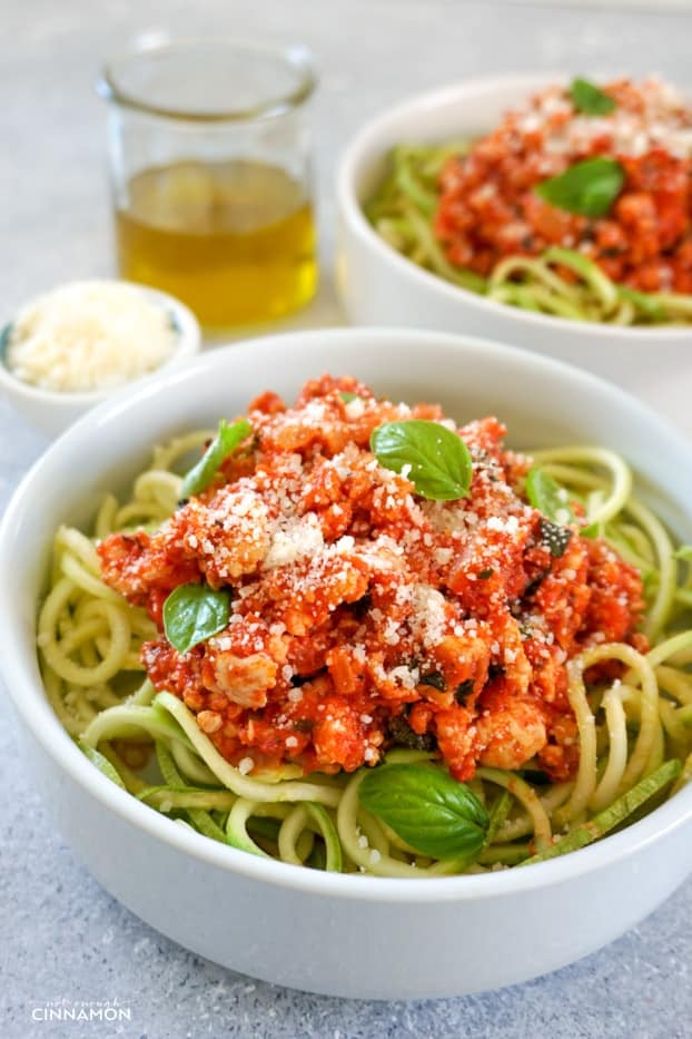 Two bowl of turkey bolognese sauce over zucchini pasta, sprinkled with grated parmesan, in two shallow round plates