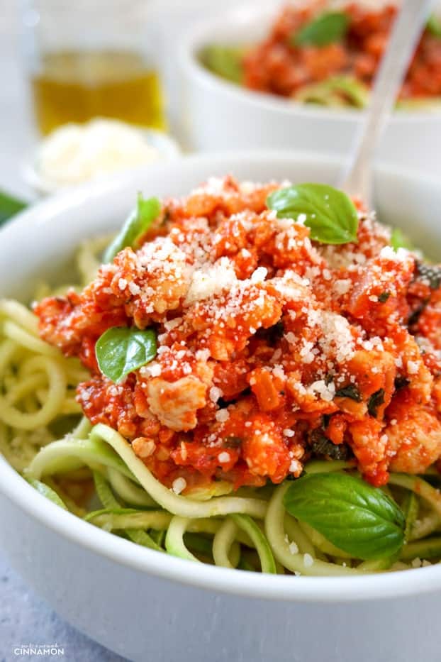 Close up on turkey bolognese sauce over zucchini pasta with fresh parmesan on top and a few fresh basil leaves