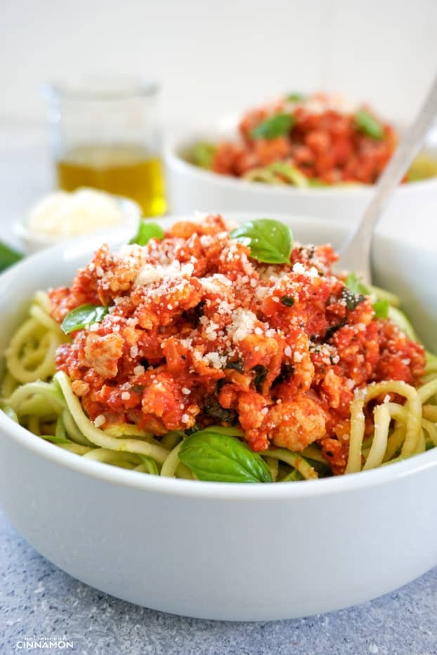 Turkey bolognese sauce on top of zucchini noodles in a white bowl, with olive oil and another bowl in the background.