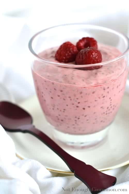 side view of vanilla raspberry chia pudding served in a dessert glass with fresh raspberries on top