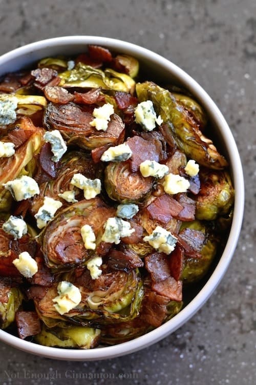 Overhead shot of Roasted Brussels Sprouts with Balsamic, Pancetta and Blue Cheese served in a white bowl with a generous sprinkling of cheese on top