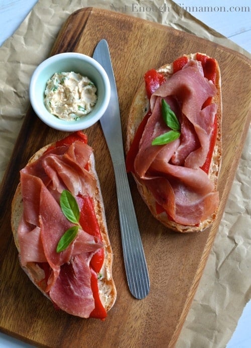 2 tartine topped with goat cheese, jamon serrano and roasted bell peppers served on a wooden board