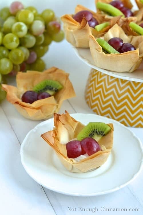 Dessert Phyllo Cups filled with ricotta, grapes and kiwi slices arranged on a cake stand and a single white plate- phyllo cups recipe