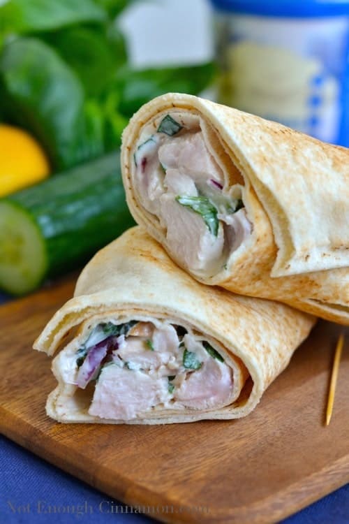 Healthy Greek Chicken Wrap cut in half and arranged on a wooden chopping board with a cucumber and fresh basil in the background