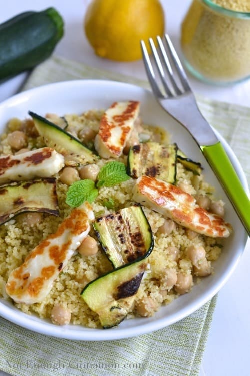 Summer Couscous Salad with chickpeas, grilled halloumi and zucchini tossed with a zesty dressing and served in a white bowl with a fork on the side