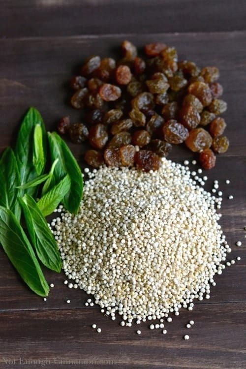 raw quinoa, mint and raisins piled up next to each other on a wooden tabletop