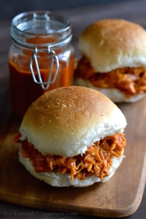 two burger buns loaded with Healthy Peach BBQ Pulled Chicken on a wooden chopping board 