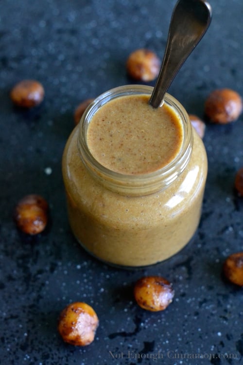 Honey Roasted Macadamia Nut Butter in a glass jar with a spoon sticking out
