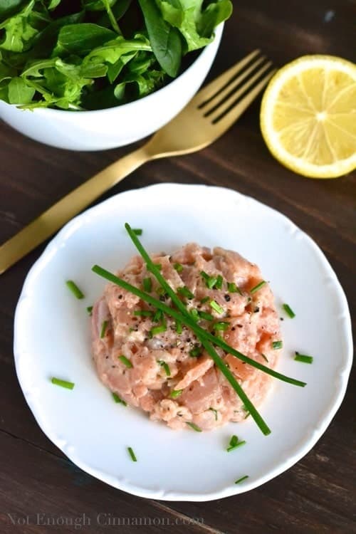 easy Salmon Tartare made from fresh and smoked salmon, served on a small white dish sprinkled with chopped chives and cracked pepper