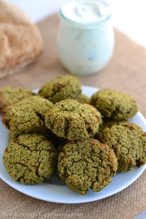 crispy oven baked falafel piled up on a small white plate with a jar of homemade yogurt sauce in the background