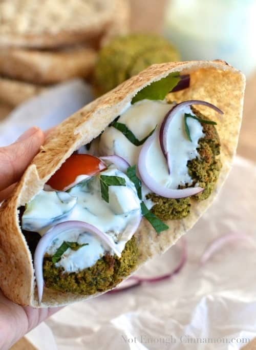 a hand holding a Baked Falafel Pita Sandwich stuffed with oven baked falafel, tomatoes, onions and a mint cucumber yogurt sauce