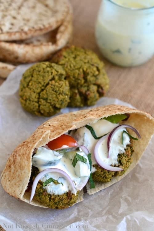Baked Falafel Pita Sandwich with yogurt mint sauce on a piece of parchment paper with some baked falafel and a jar with more sauce in the background