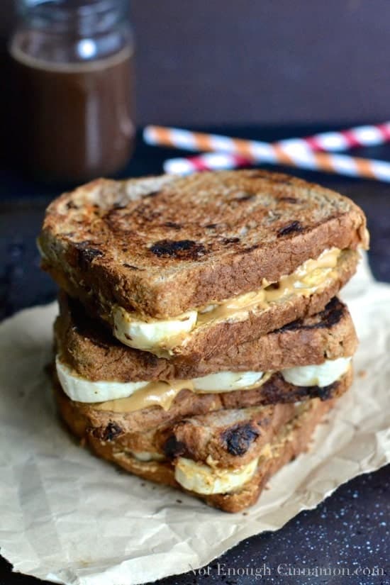 a stack of Peanut Butter and Banana Sandwiches with a jar of homemade peanut butter chocolate sauce and some straws in the background