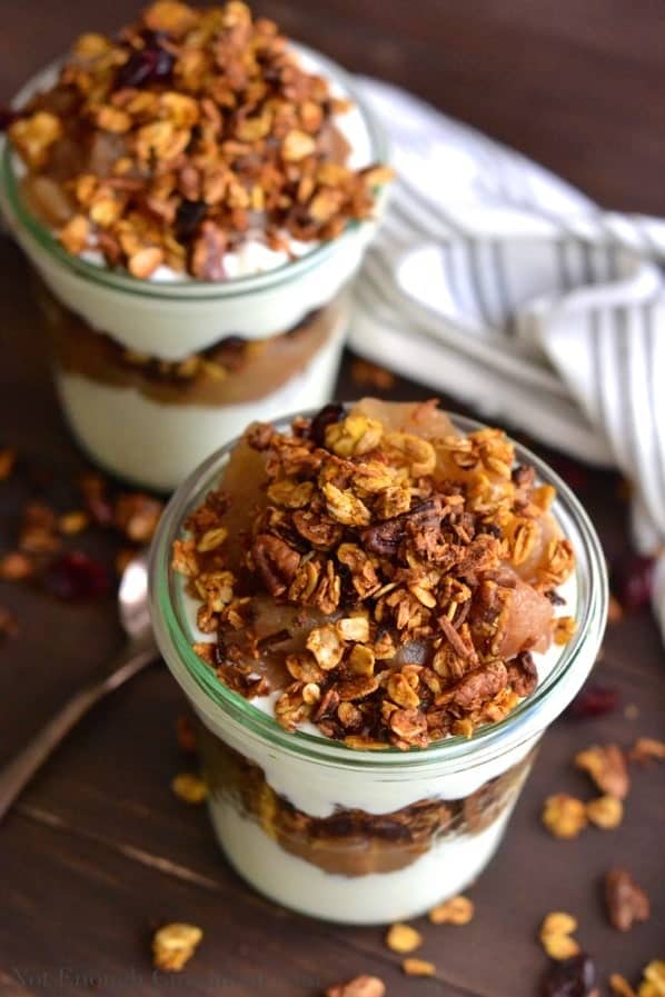 Homemade Pumpkin Granola and Apple Yogurt Parfaits served in two glass jars on a rustic wooden table