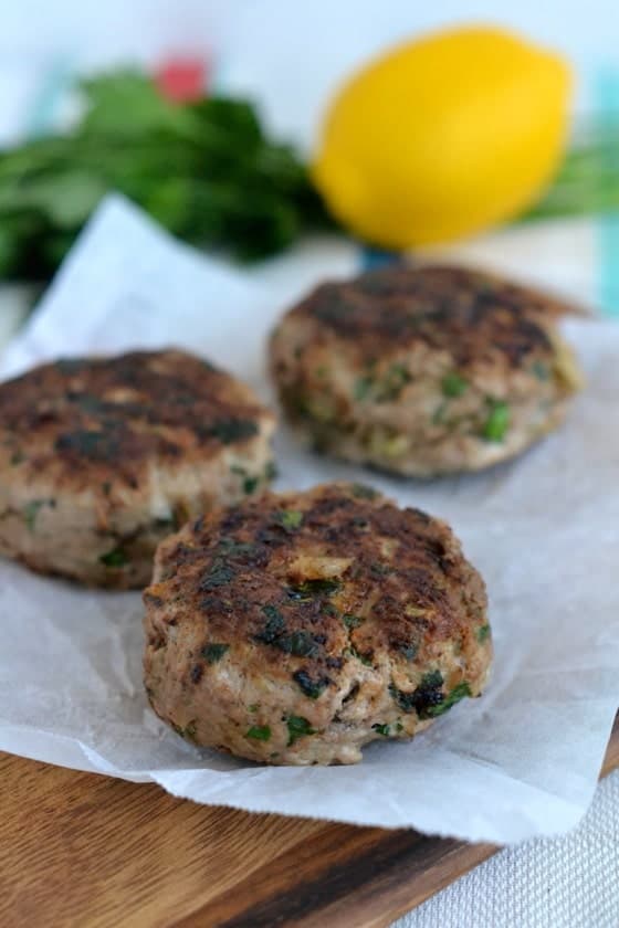 Middle Eastern Lamb Burger patties with mint arranged on a sheet of parchment paper with fresh herbs and a lemon in the background - lamb burger recipe