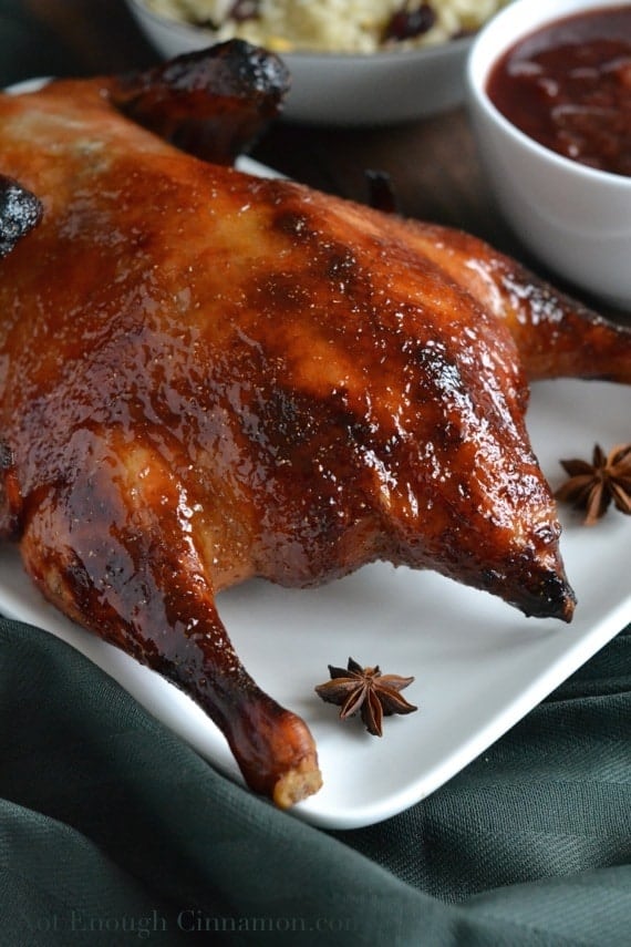 Close-up of Easy Plum and Ginger Chinese Roasted Duck served on a big white platter with whole star anise as decorations and a small side dish with plum sauce in the background