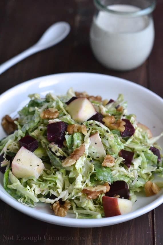 Chopped Brussels Sprout Salad topped with chopped walnuts, apples and beets served in a shallow white salad bowl with Skinny Blue Cheese Dressing in the background