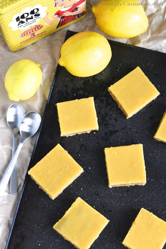 overhead shot of gluten-free easy lemon bars arranged on a black baking tray with some lemons in the background