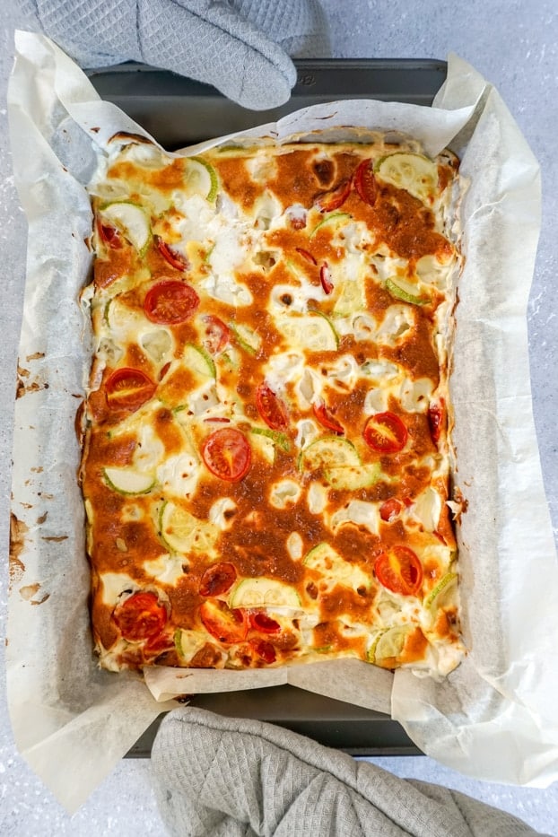 A pan of baked frittata held with two grey potholders 