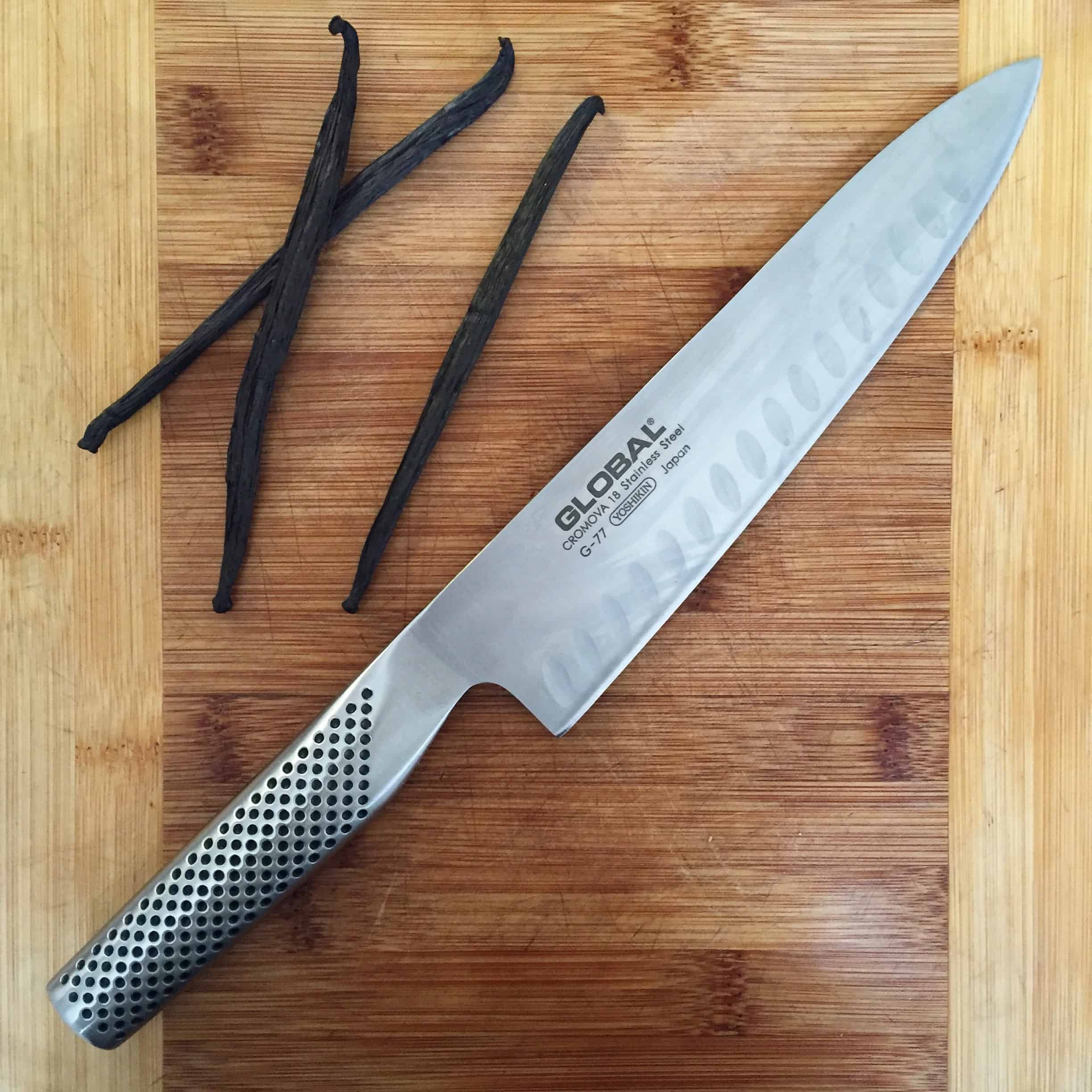 a sharp Japanese knife on a cutting board with three vanilla beans on the side