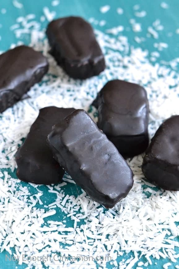 Easy Homemade Vegan and Paleo Bounty Bars arranged on a blue tabletop with shredded coconut surrounding them