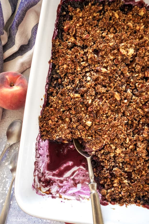 A dish of blueberry peach crisp with a silver serving spoon in it.