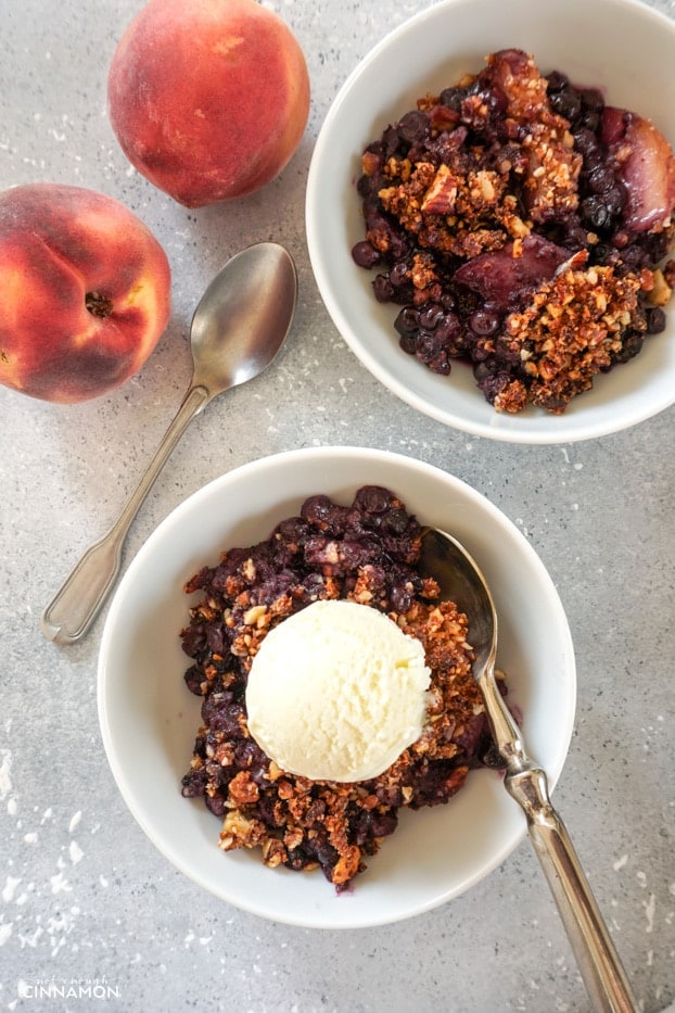Two bowls of blueberry peach crisp with an ice cream scoop.