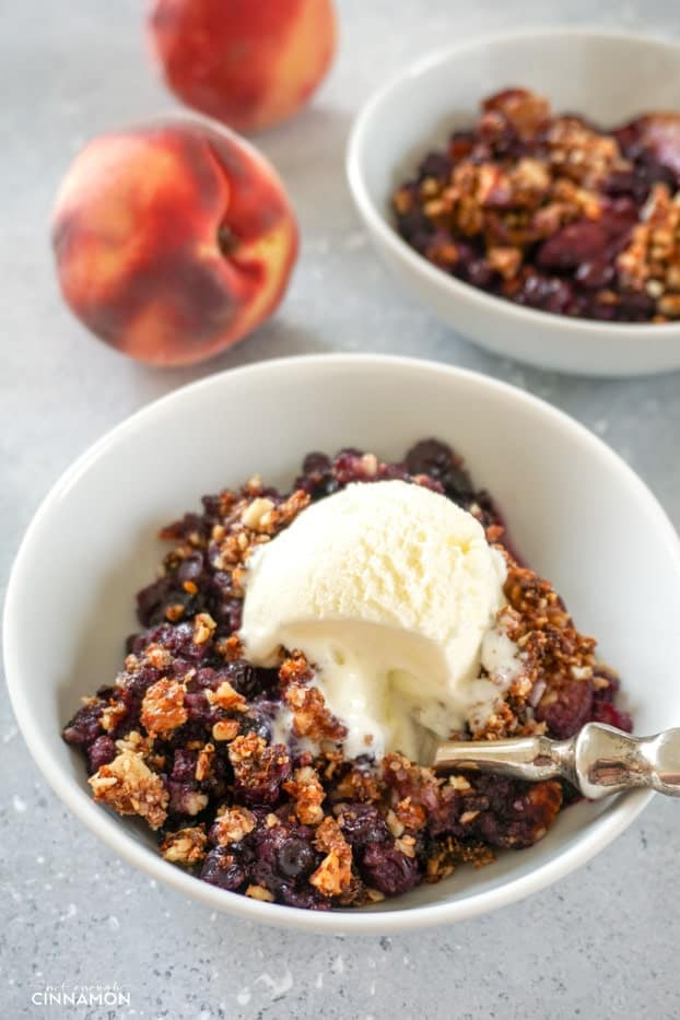 blueberry peach crisp in a white bowl topped with ice cream