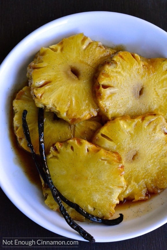 slices of Roasted Pineapple with Honey and Salted Butter Caramel on a plate with some vanilla beans on the side