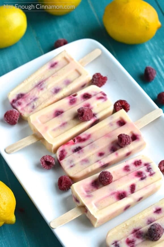 overhead shot of Skinny Lemon Curd and Raspberry Popsicles on a white plate with frozen raspberries and fresh lemons on the side