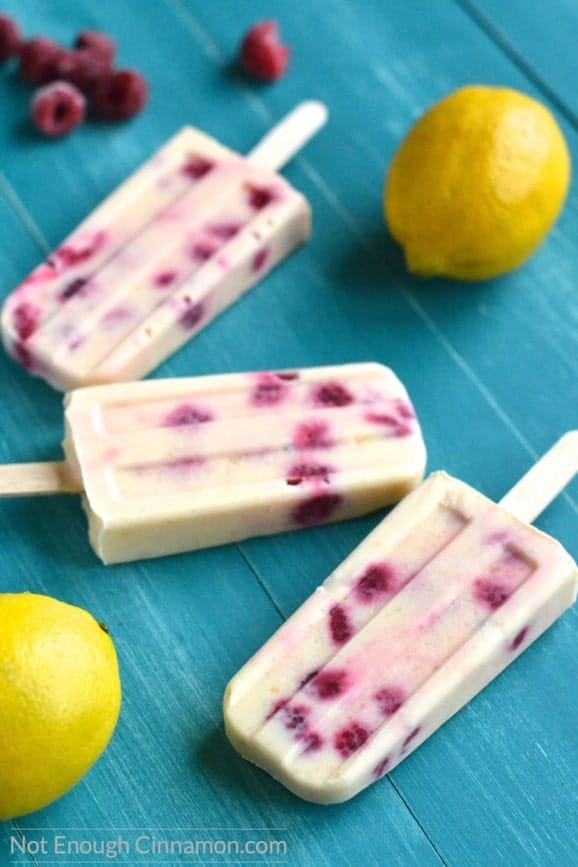close-up of Skinny Lemon Curd and Raspberry Popsicles on a rustic blue tabletop with raspberries and lemons on the side