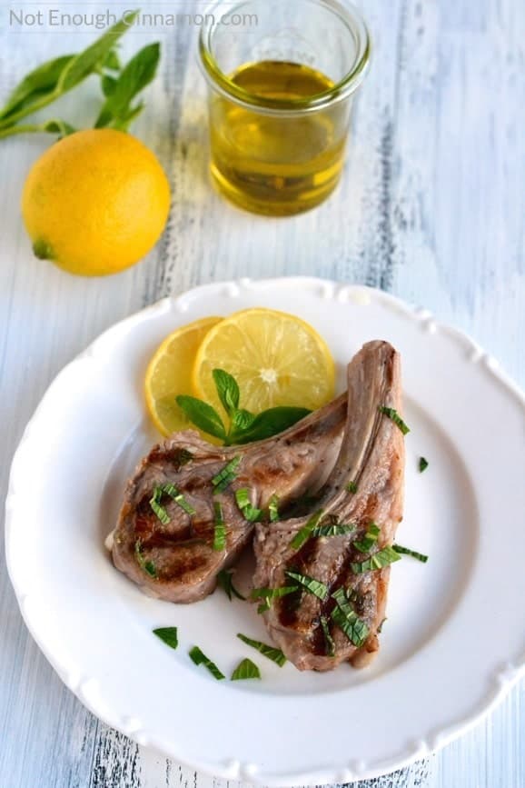 easy paleo pan-fried Lamb chops in lemon mint marinade on a white plate with lemon and mint leaves on the side