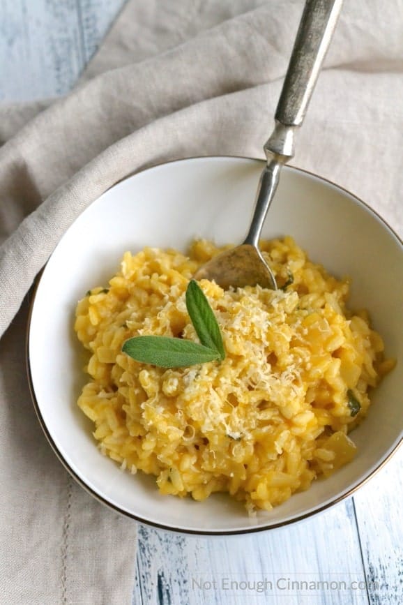 overhead shot of easy pumpkin risotto in a white bowl with a spoon and a beige napkin on the side
