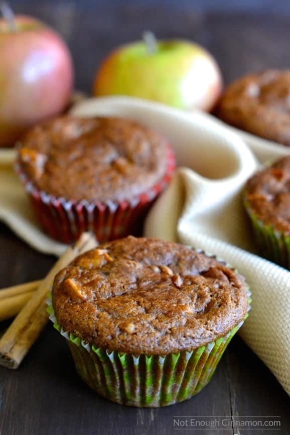 close-up of healthy apple spice muffin in a green muffin liner with more muffins and apples in the background 