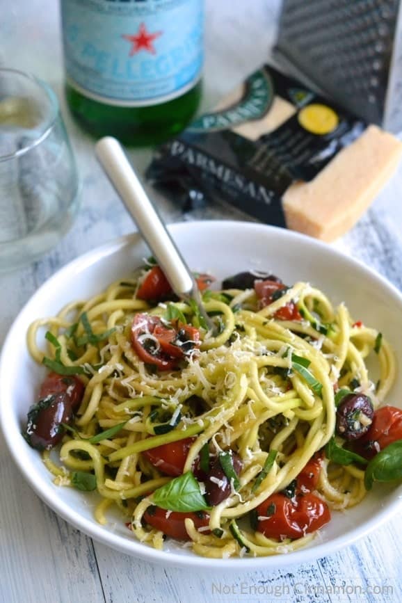 a fork twirling zucchini noodles alla puttanesca in a white bowl (zoodles recipe) 