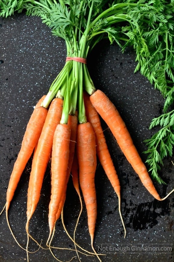 a bunch of fresh carrots on a dark tabletop ready to be roasted