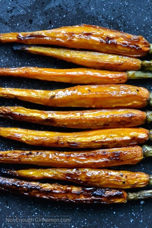 caramelized balsamic roasted carrots lined up horizontally on a dark tabletop