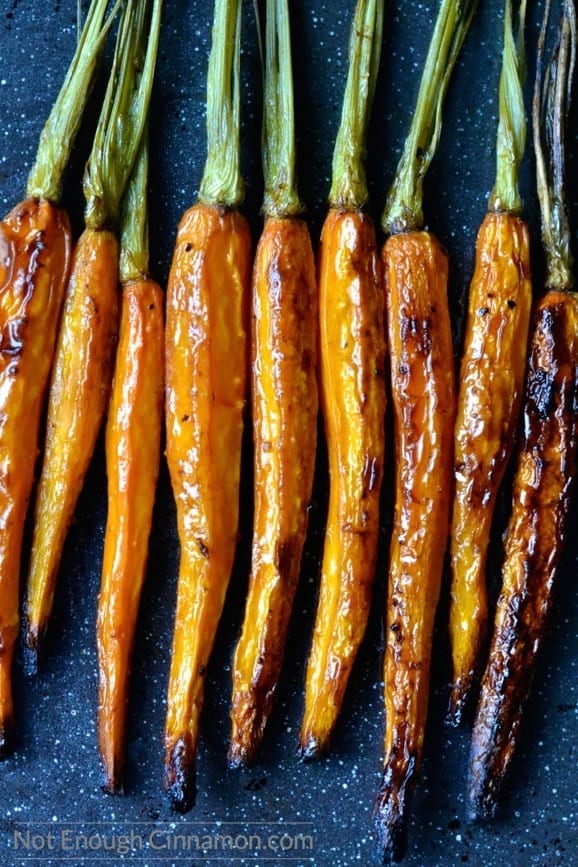 lightly charred, whole balsamic roasted carrots lined up next to each other on a dark tabletop