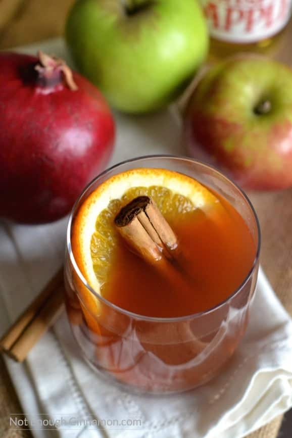 overhead shot of a glass of pomegranate spiced apple cider with pomegranates and apples in the background