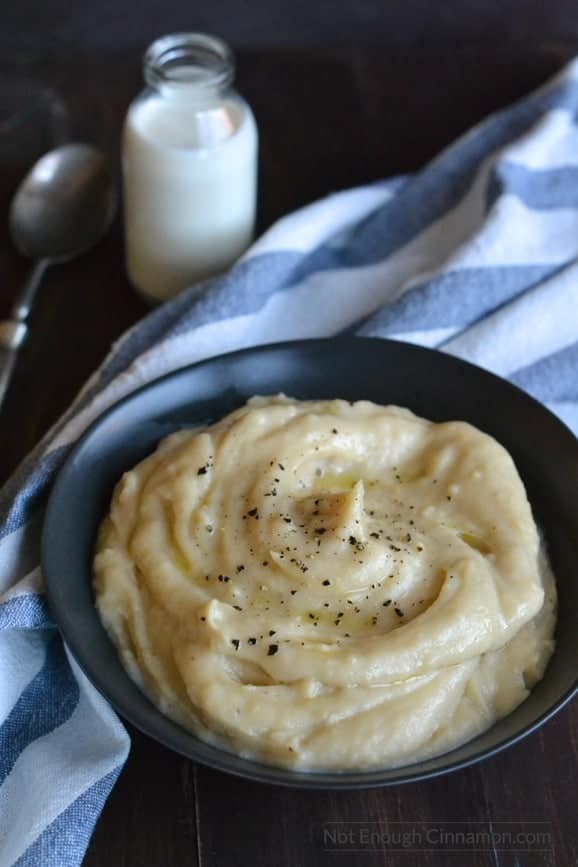 close-up of a bowl of slow cooker mashed potatoes with goat cheese with a striped cloth napkin and a bottle of milk in the background